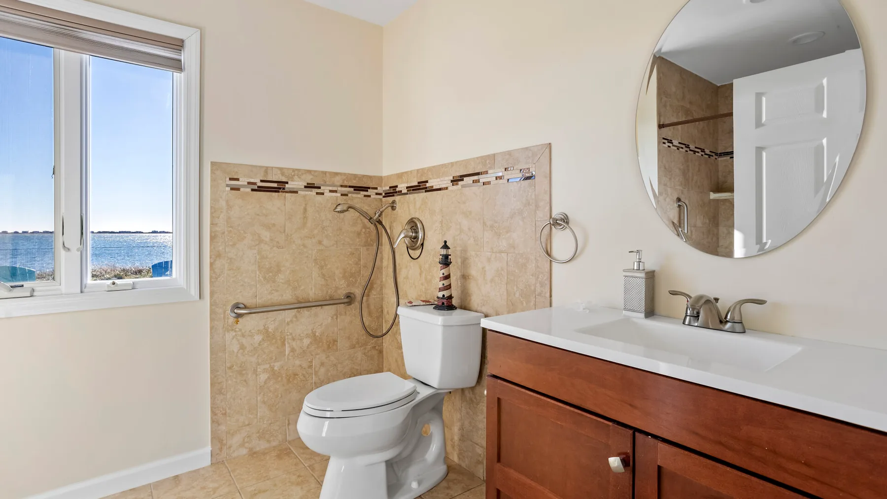 A bathroom with a vanity, toilet, and shower beside a window overlooking the water.
