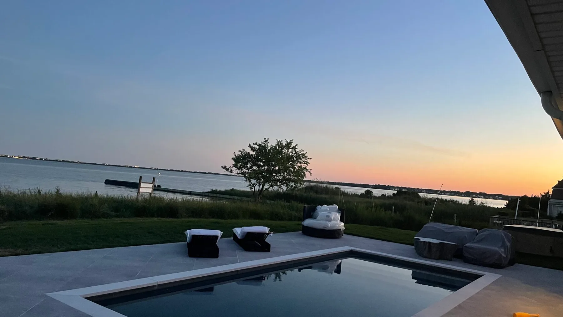An outdoor swimming pool overlooks a calm body of water at sunset.