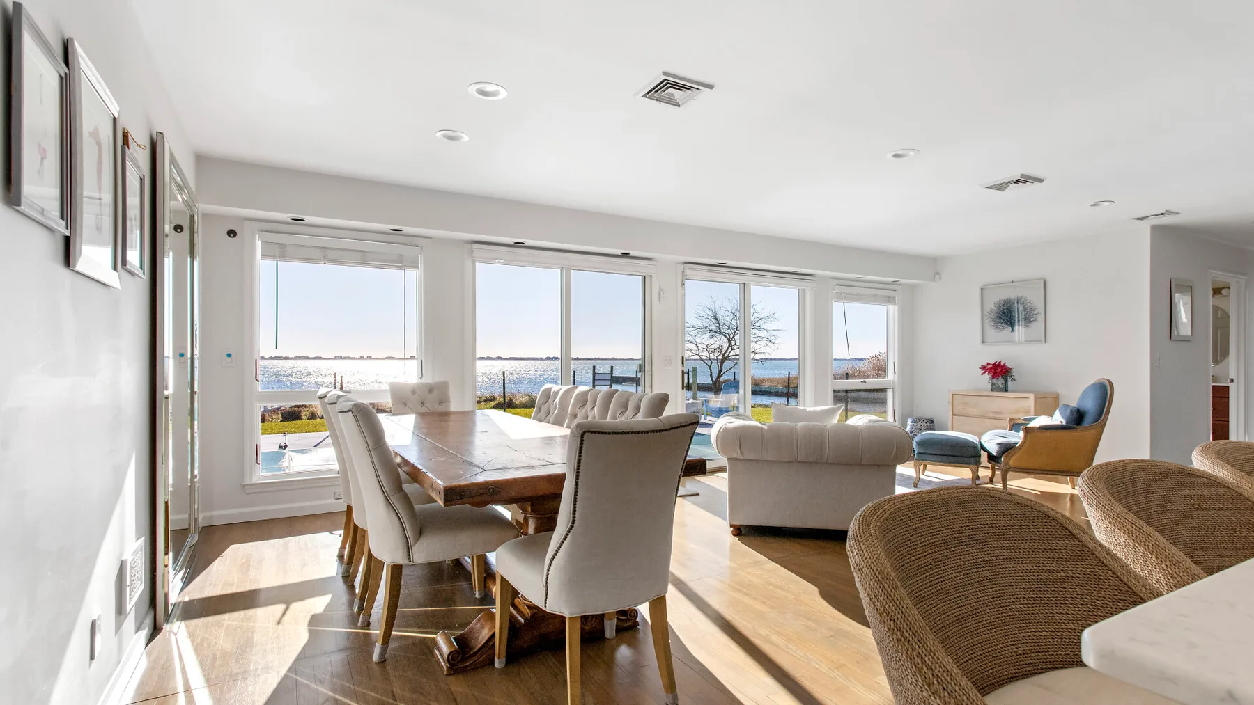 Bright living and dining area with seating and large windows overlooking the water.