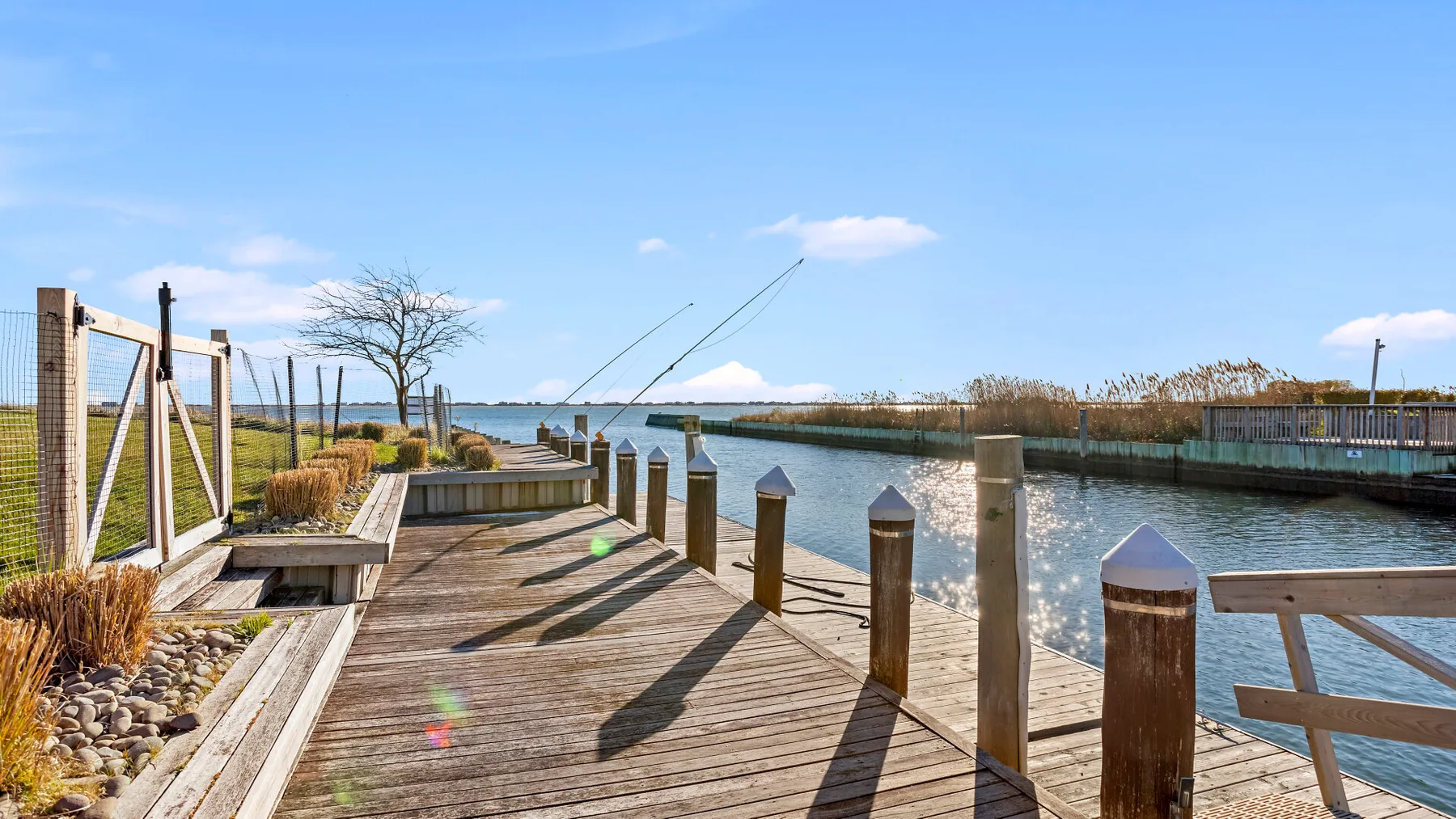 A wooden waterfront deck borders a calm inlet beneath a clear blue sky.