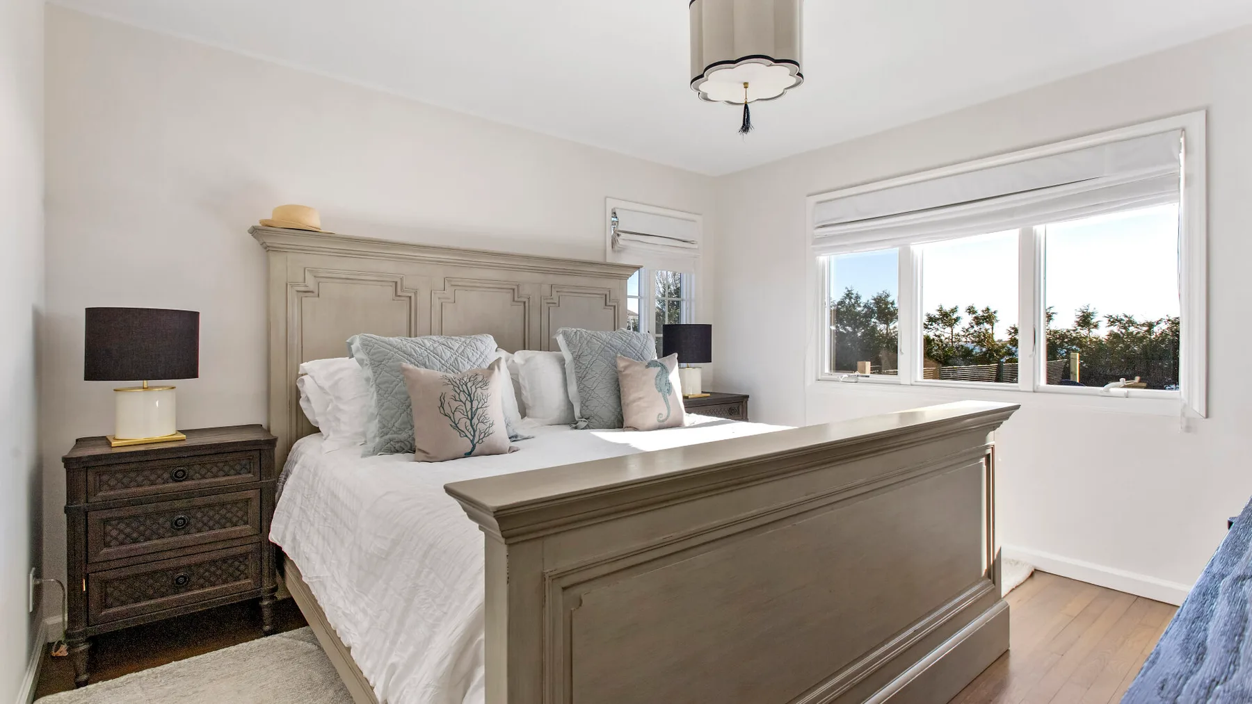 A bright bedroom with a large bed and a wide window overlooking trees.