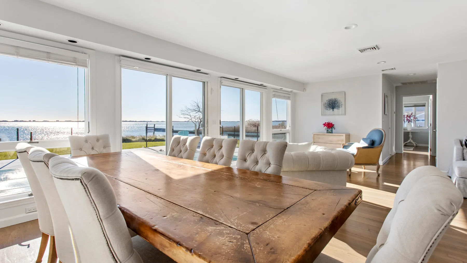 A bright dining area with a large wooden table and broad windows overlooking the water.