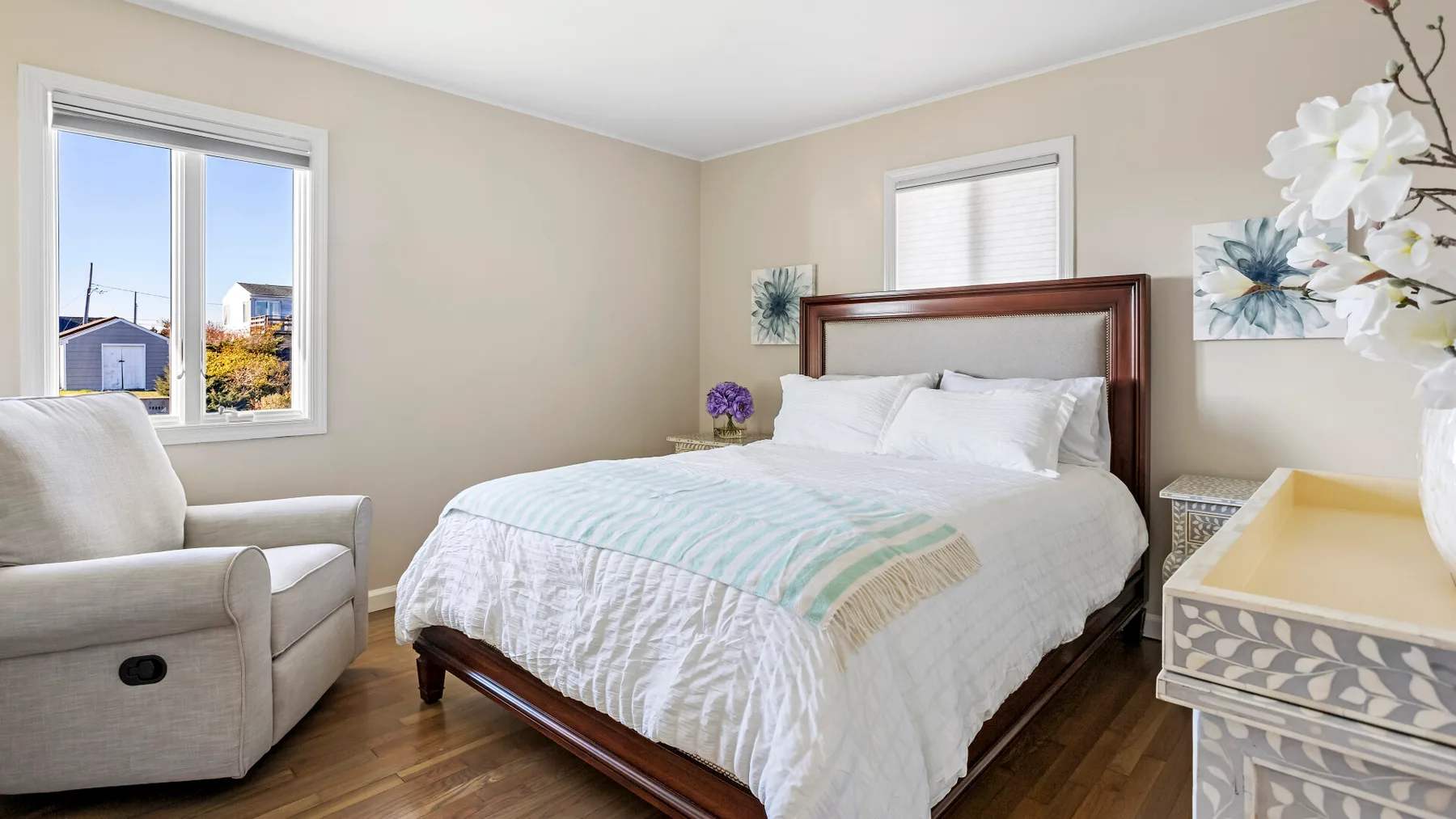 A bedroom with a bed, an upholstered chair, and windows.