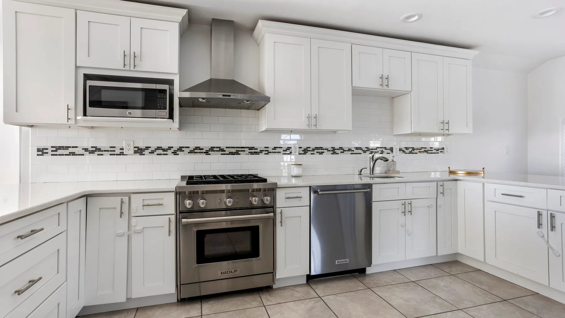 A bright kitchen with white cabinets, a stove, and a tiled backsplash.