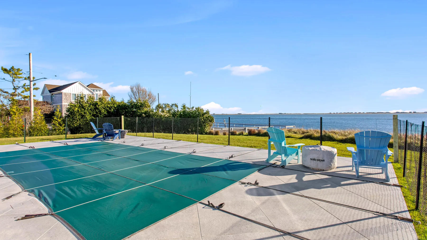 An outdoor tennis court beside the water, with seating along the edge.