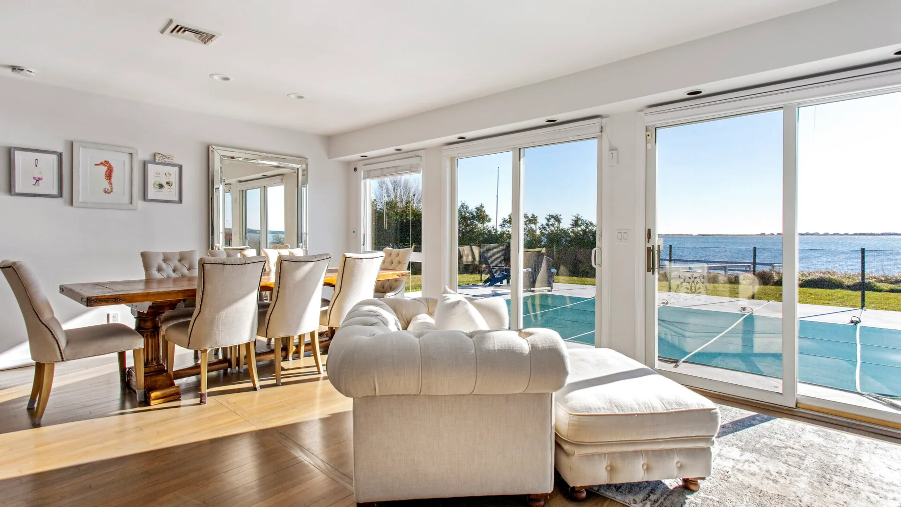 A bright living and dining area opens onto a patio with a pool and ocean view.