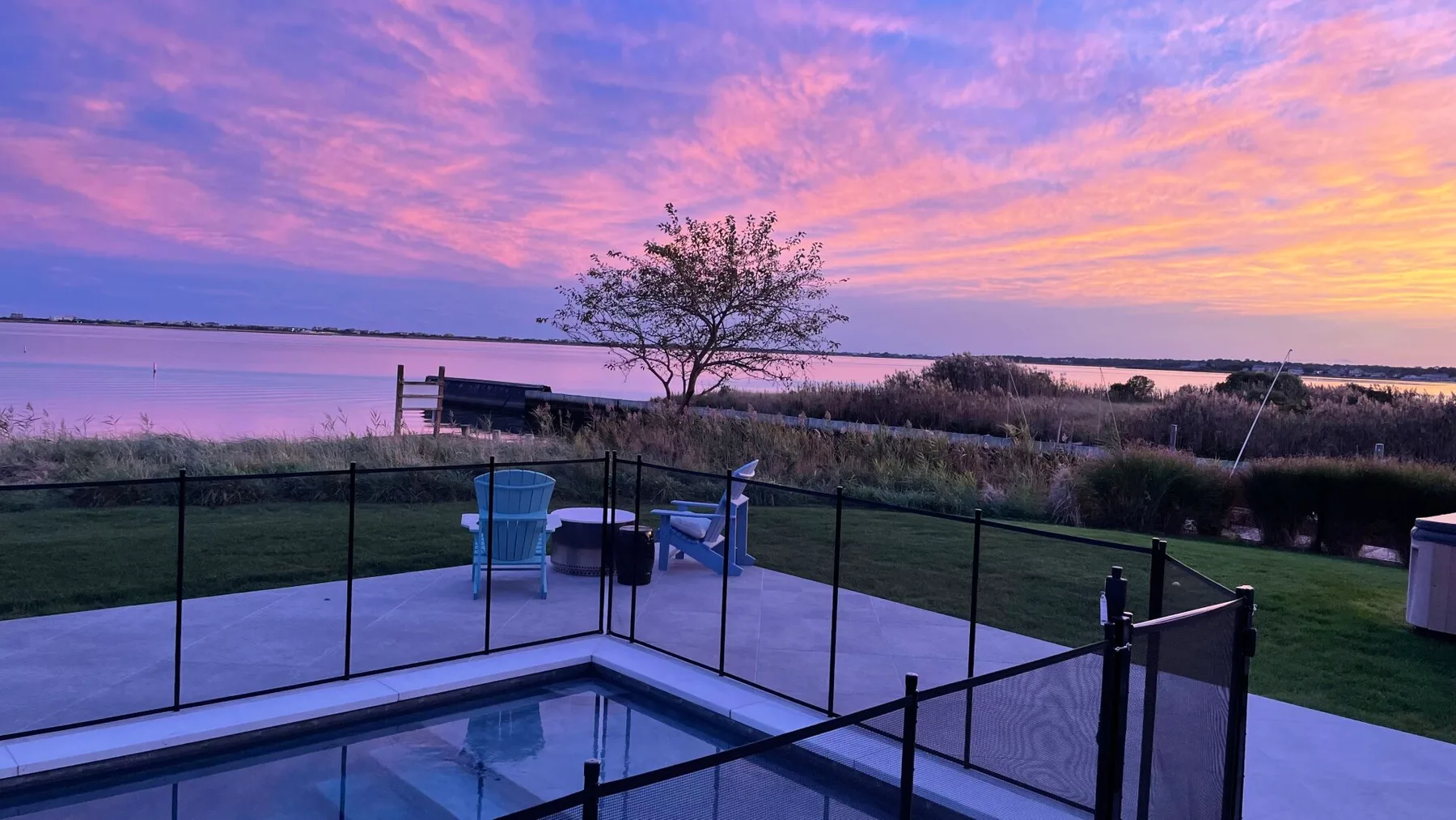 A fenced patio overlooks a lake beneath a colorful sunset sky.