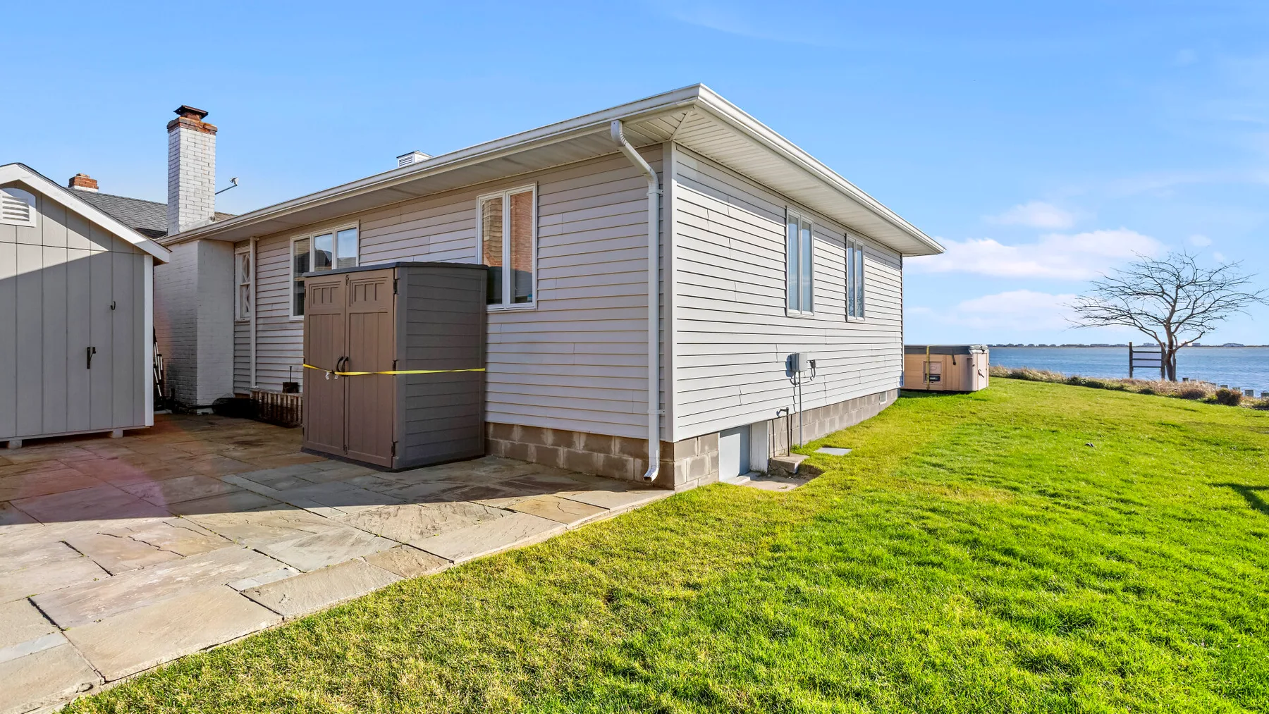 A light-sided house borders a paved patio and a grassy lawn.