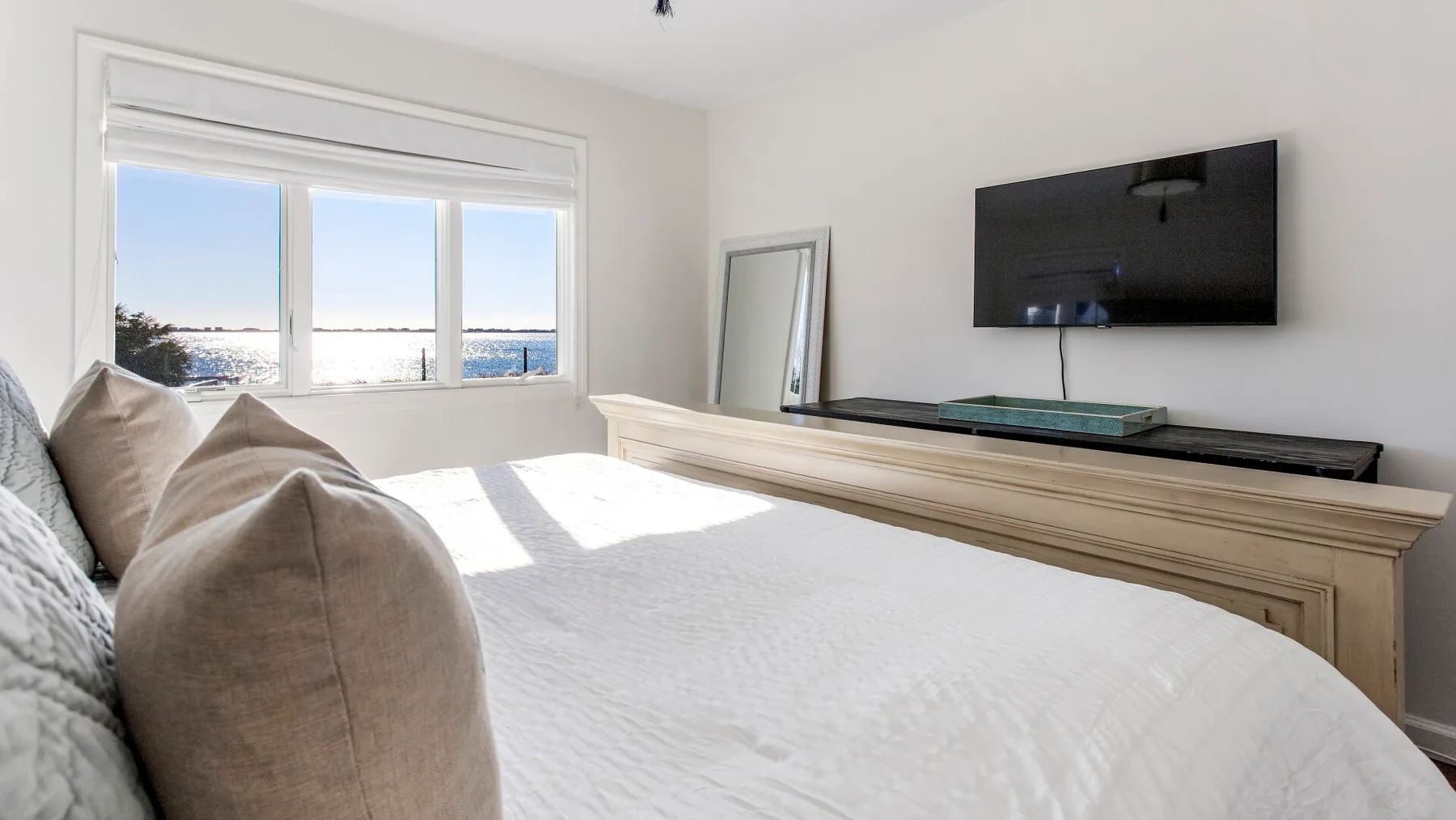 A bright bedroom with a bed, large windows, and a wall-mounted television.