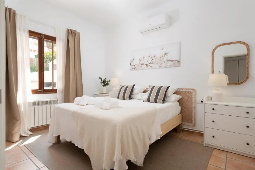 A bright bedroom with a double bed, striped pillows, and a window with curtains.