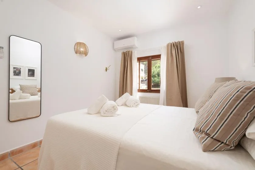 A bright bedroom with a neatly made bed and a window framed by curtains.