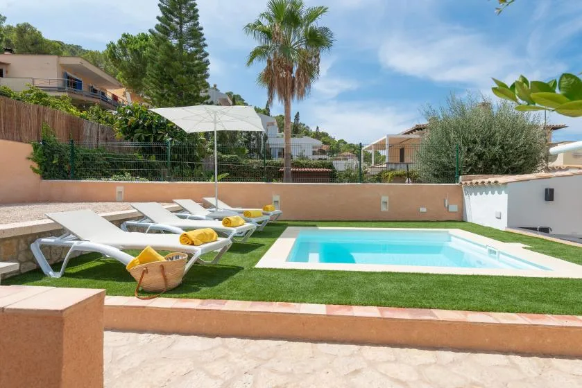 An outdoor swimming pool sits beside lawn, lounge seating, and a shade umbrella.