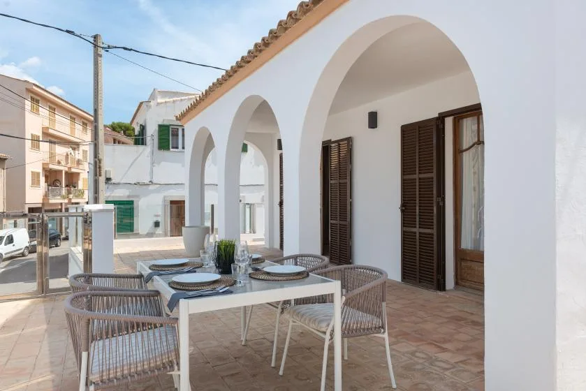 A shaded outdoor dining area sits beneath a row of white arches.