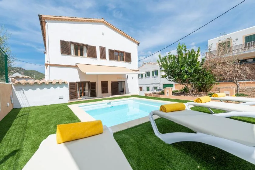 A backyard pool beside a white house, with sun loungers on the grass.