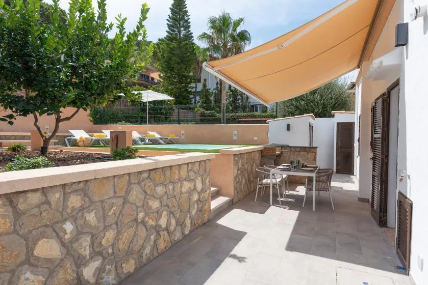A shaded outdoor patio with a dining table beside a stone wall.