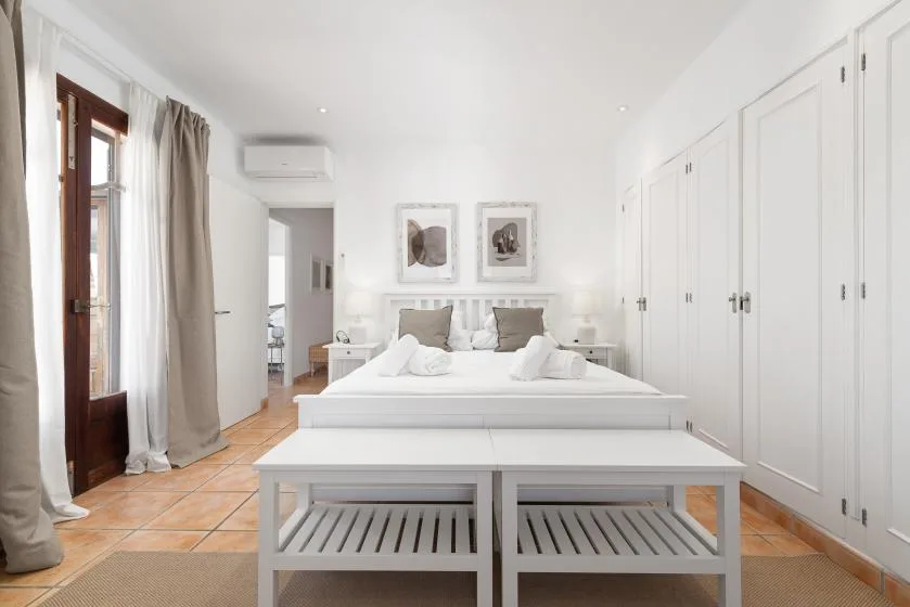 A bright bedroom with a bed, bedside tables, and built-in wardrobes.