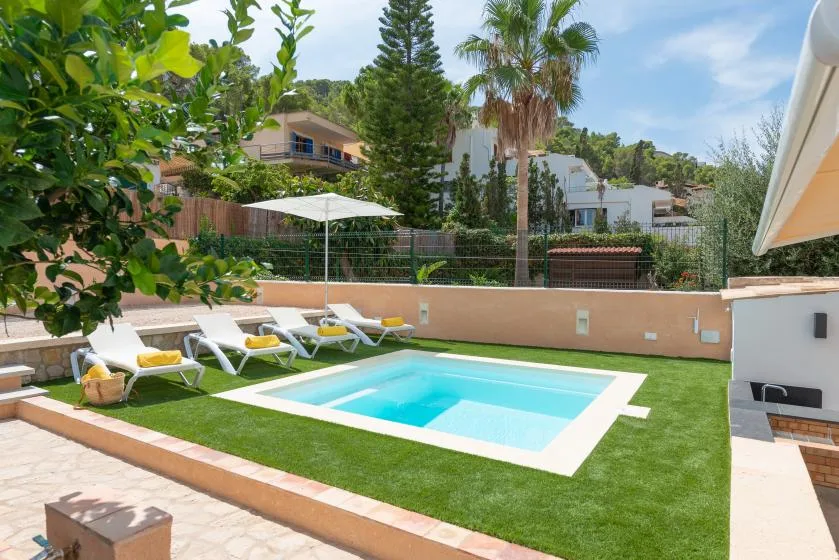 A sunny outdoor pool area with lawn, lounge seating, and a patio umbrella.