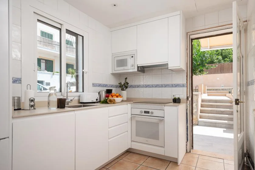 A bright white kitchen with countertop appliances and an open door to an outdoor patio.
