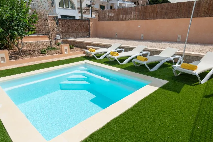 An outdoor swimming pool is surrounded by artificial turf and white lounge seating.