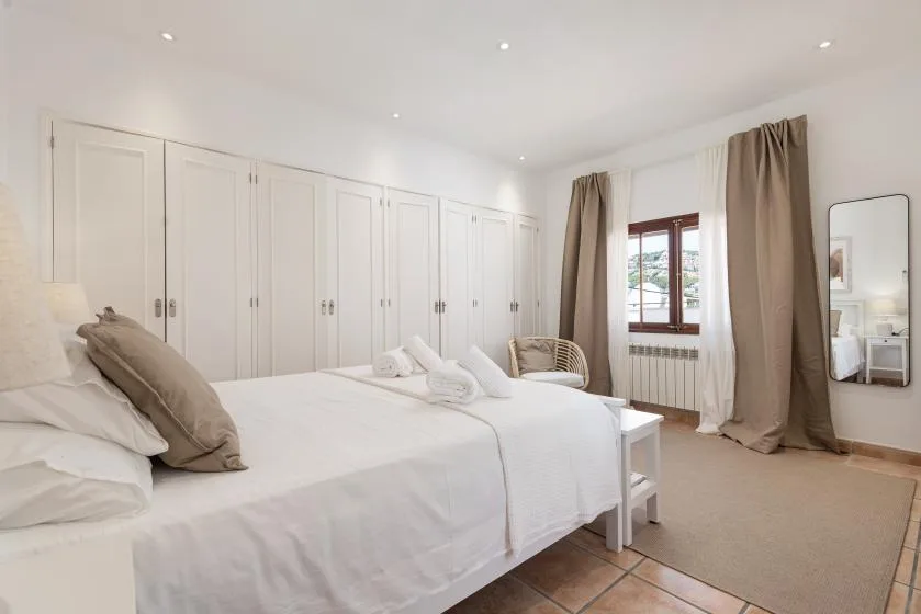 A bright bedroom with a neatly made bed and built-in cupboards.