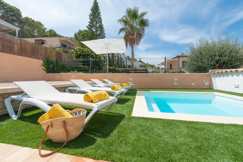 An outdoor swimming pool beside lounge seating on a grassy patio.