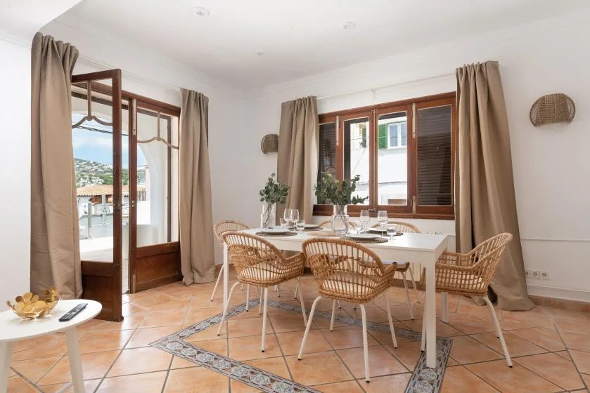 A bright dining area with a table and woven seating beside large windows.