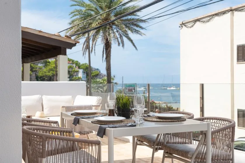 Una terraza al aire libre con mesa y asientos tejidos ofrece vistas al mar.