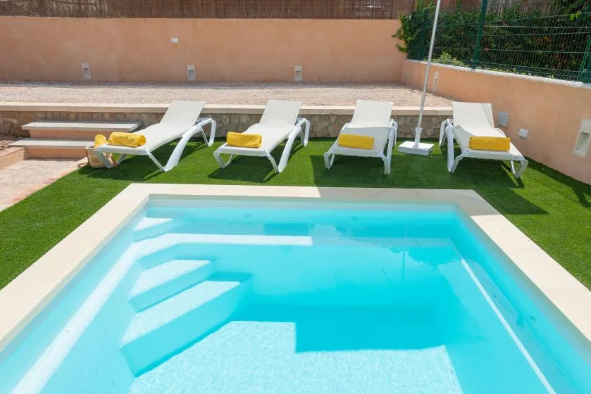 Una pequeña piscina al aire libre con escalones está junto a varias tumbonas.