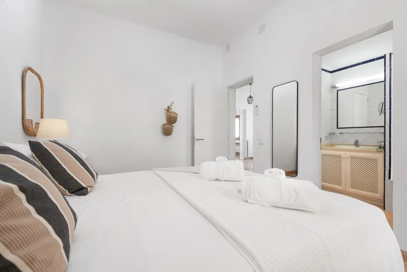 A bright bedroom with neatly made beds and a bathroom visible through the doorway.