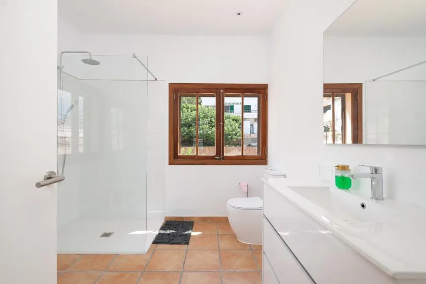A bright bathroom with a glass shower, a sink, and a window.