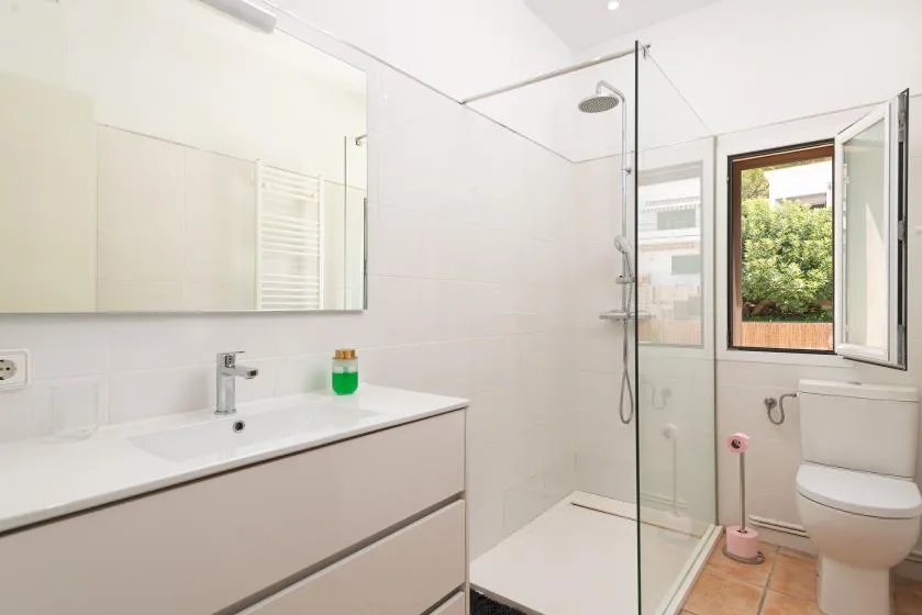 A bright bathroom with a vanity, glass shower, and window.