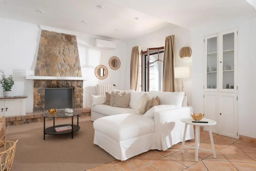 A bright living room with white seating arranged around a stone fireplace.