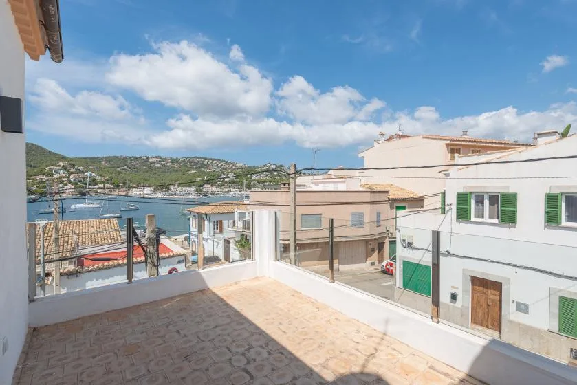 A sunny terrace overlooks nearby buildings and a bay beneath a partly cloudy sky.