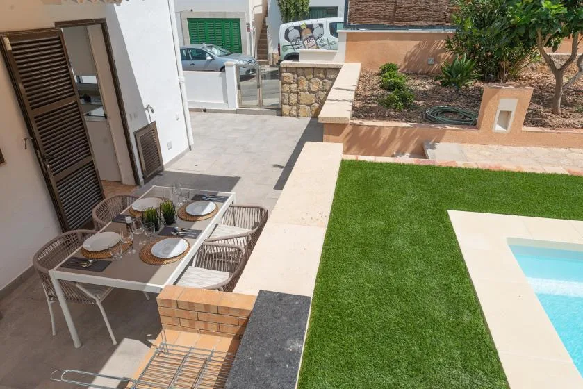 A patio dining area beside a green lawn and the edge of a swimming pool.