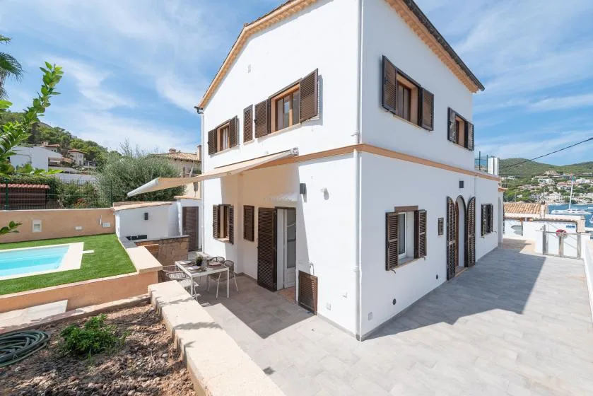 Una casa blanca de dos plantas con ventanas de marcos marrones junto a una piscina.