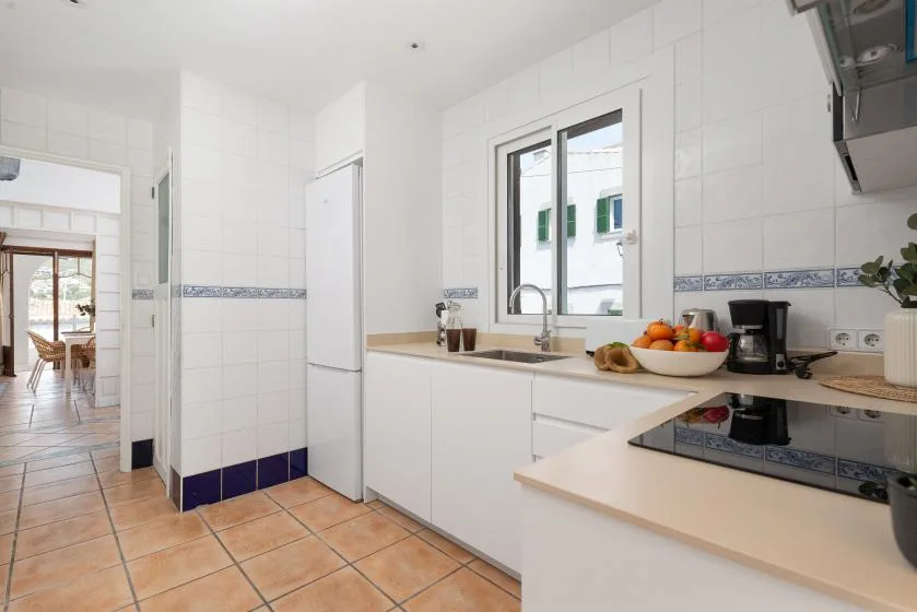 A bright tiled kitchen with white cabinets, a sink, and a countertop cooktop.