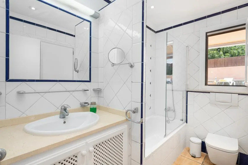 A bright tiled bathroom with a sink, bathtub, and window.