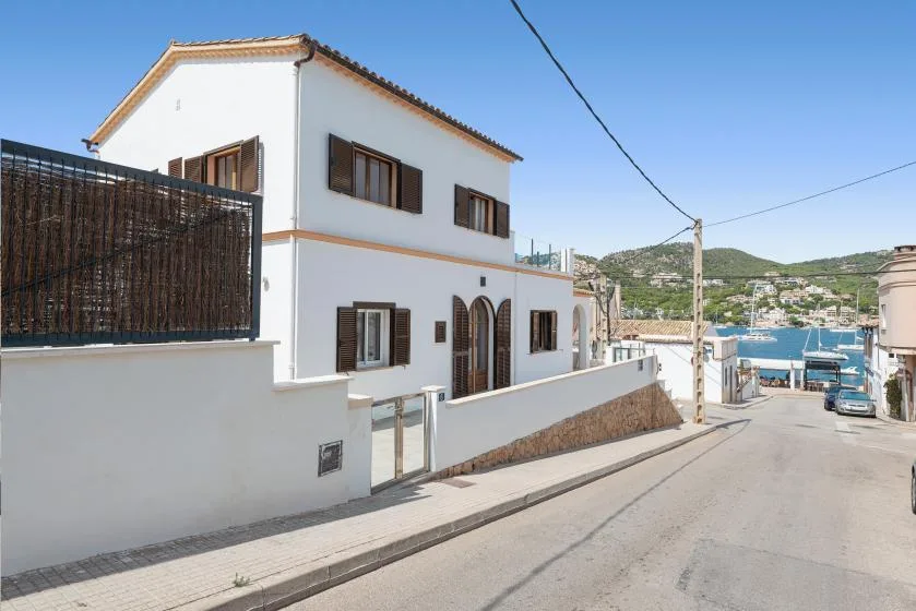 A white two-story house stands beside a sloping street overlooking the coast.