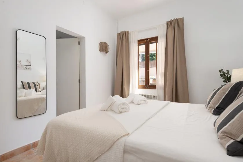 A bright bedroom with a neatly made bed and a window framed by curtains.