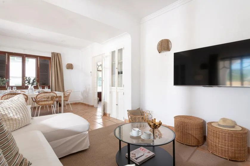 A bright living room has seating, a glass coffee table, and a wall-mounted television.