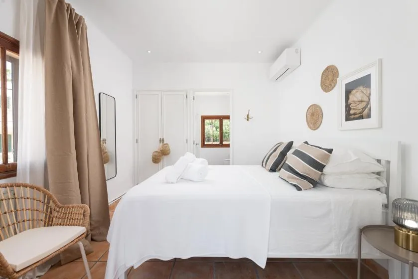 A bright bedroom with white bedding and striped accent pillows.
