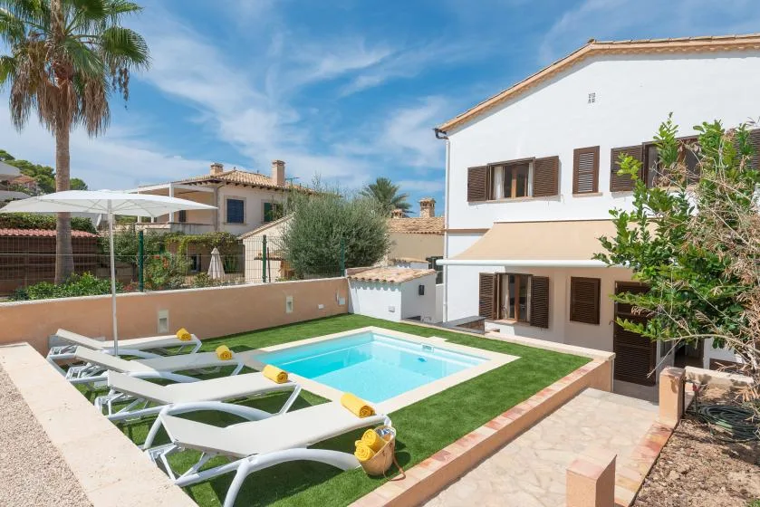 A swimming pool and sun loungers sit beside a white two-story house.