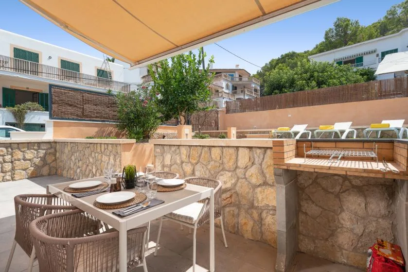 An outdoor dining area sits beneath a tan awning beside a stone terrace wall.