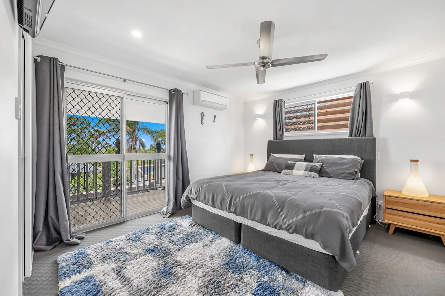 A bedroom with a gray bed, curtained windows, and a patterned rug.