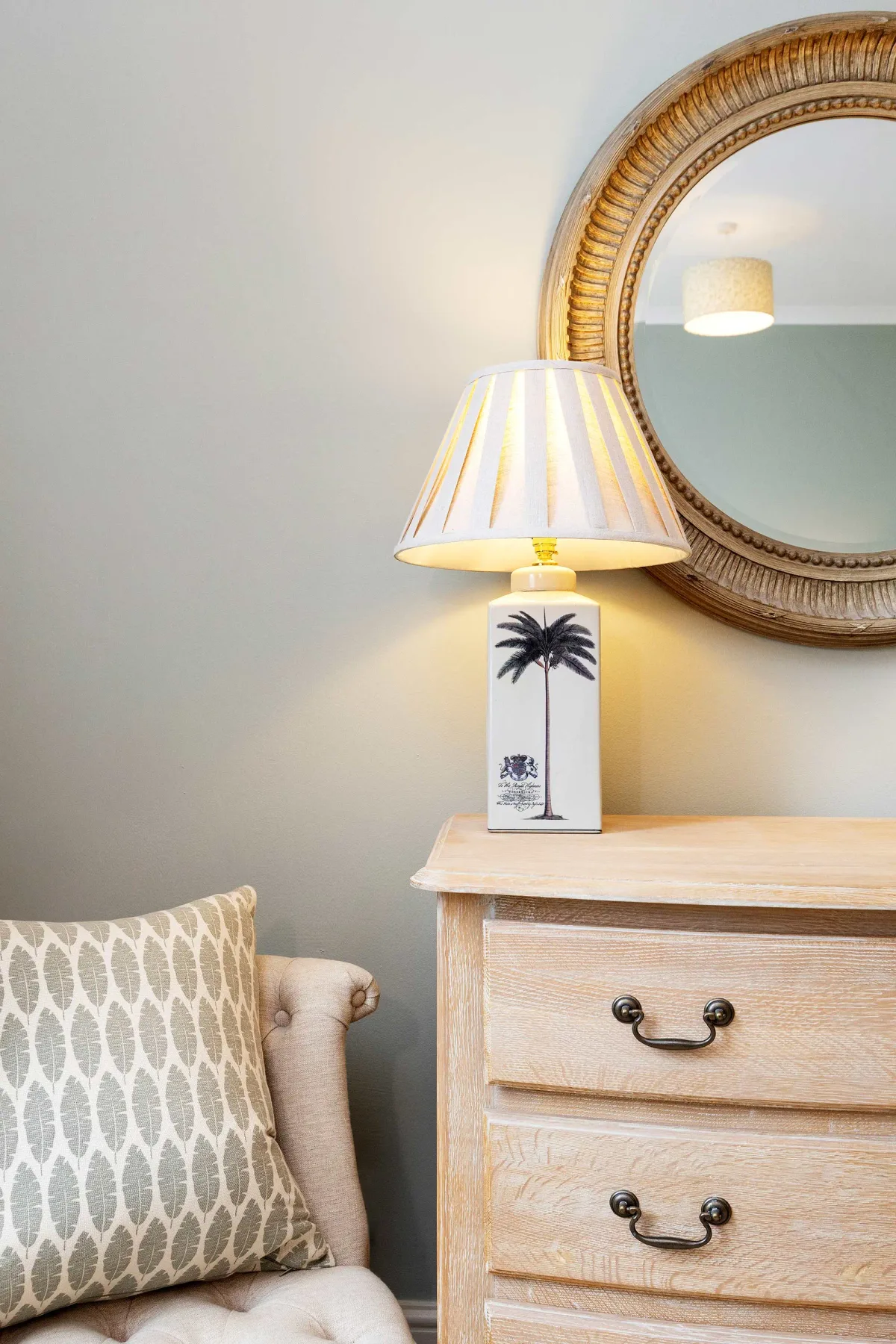 Una cómoda de dormitorio con una lámpara de mesa y un espejo redondo.