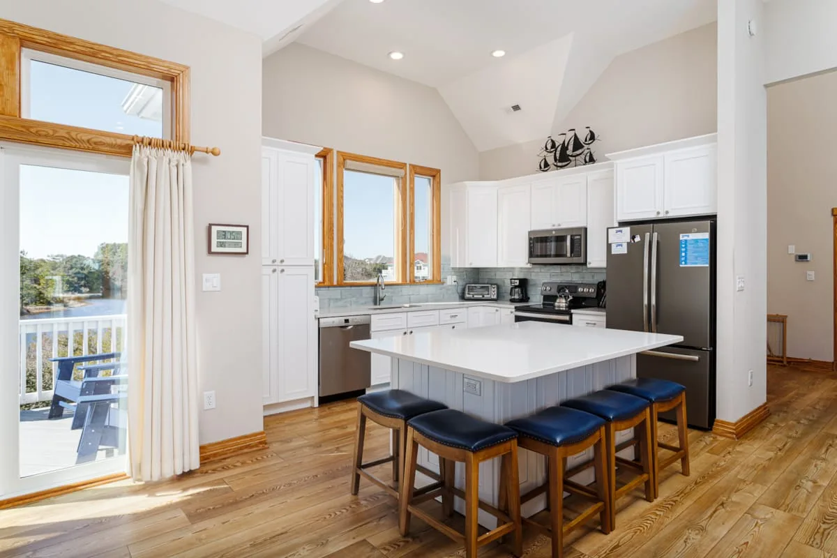 A bright kitchen with a central island, bar seating, and large windows.