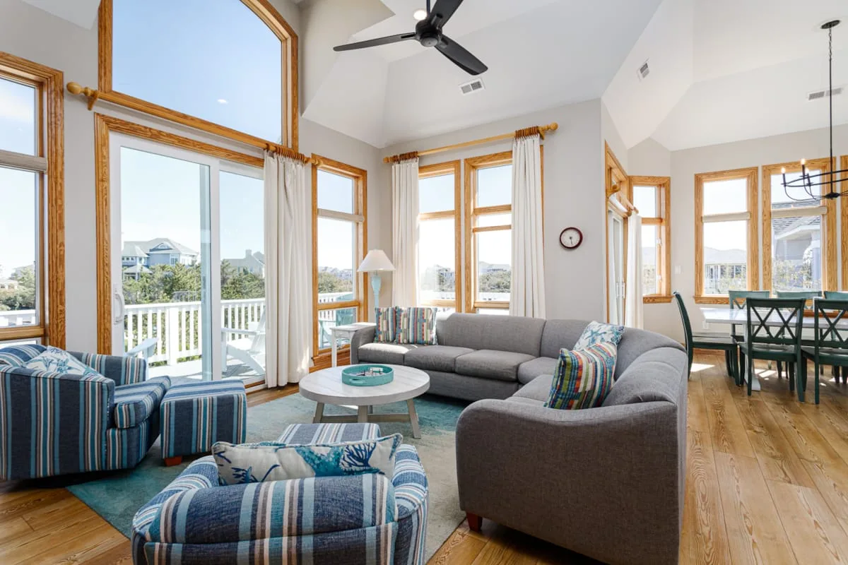 A bright living room with a gray sectional, striped seating, and large windows.