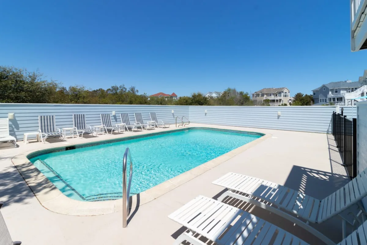 An outdoor swimming pool is surrounded by lounge chairs and a pale deck.