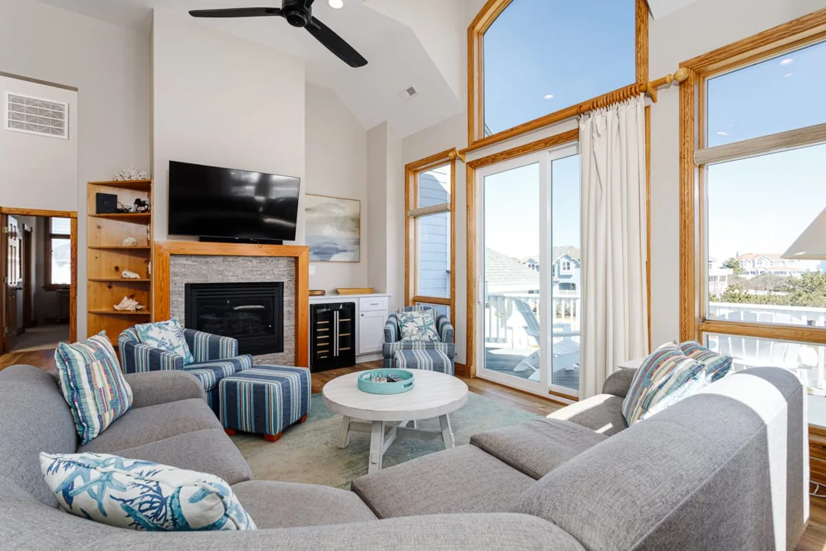 A bright living room with seating arranged around a fireplace and large windows.