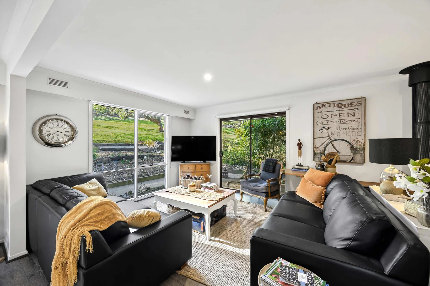 A bright living room with black seating around a coffee table and large windows.